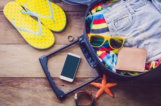 Clothing traveler's , wallet, smart phone devices, on a wooden floor in the luggage ready to travel.