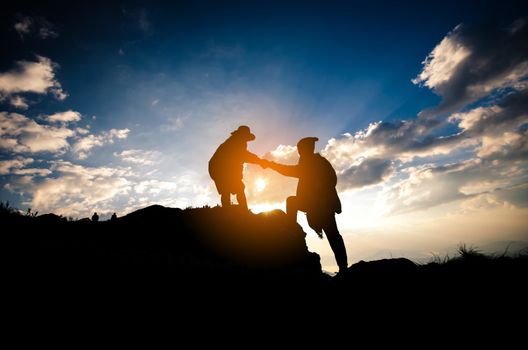 Silhouette of people helping person on the mountain at morning