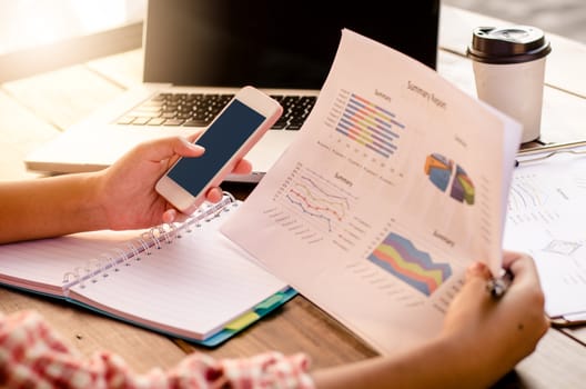 Businessman holding paperwork and smart phone on the table and analyzing investment chart working in office. Business work concept.