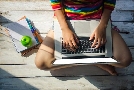 Young girls are using a laptop on a wooden floor. and sunshine