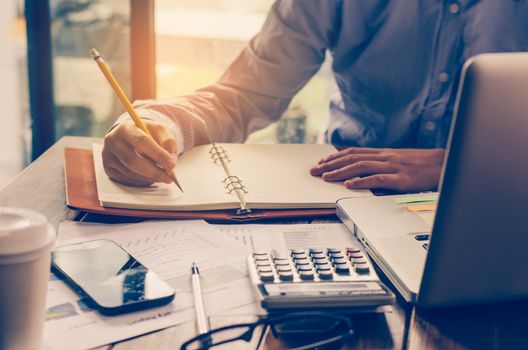 Businessman holding smart phone and work with laptop on the table and analyzing investment chart working in office. Business work concept. 
