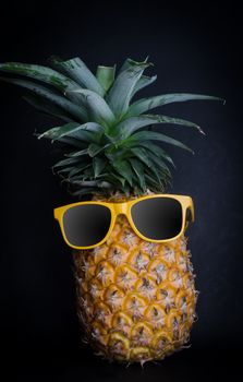 Pineapple sunglasses resting on the black background concept for travel.