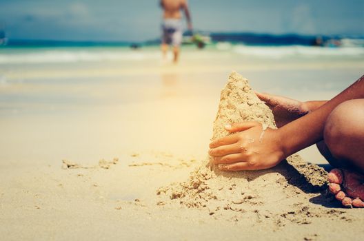 The child is sitting in the sand beside the sea.