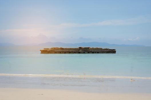 The sea is clear with the remains of the building in the middle of the water.
