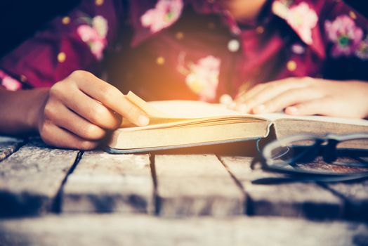 Focus hand open book for reading on wooden table with gold lighting at the morning 