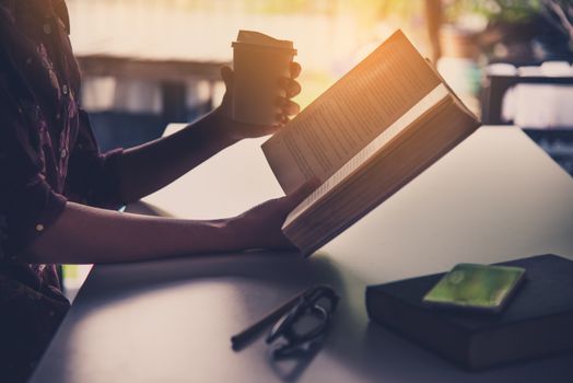 The hand of a businessman holding a cup of coffee and reading a book during leisure time.