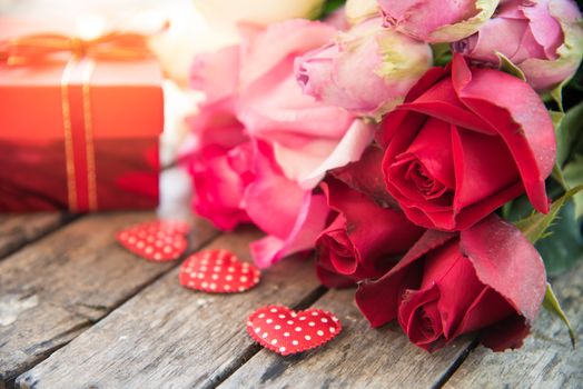 Red gift boxes, red hearts and roses are placed on a wooden floor.