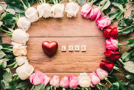 Colorful roses lined up on a wooden floor with heart and word "LOVE" - concept for love