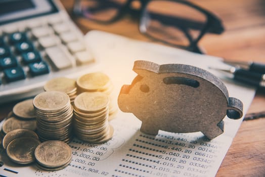 Coins are placed on the area with the sign of piggy bank overlaid on the area of the working table with a laptop. - The concept of saving money 