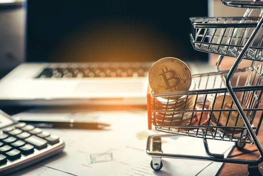 Bitcoin in mini shopping cart on table for work and laptop for work to shopping online concept 