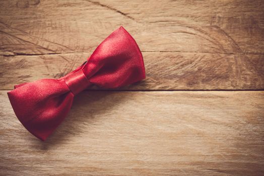 Red bow tie placed on wooden floor.