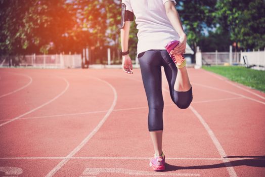 The female runner is warming up before jogging in the field.