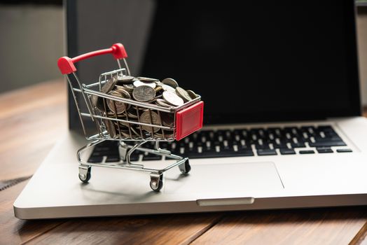 coin in mini shopping cart on table for work and laptop for work to shopping online concept 