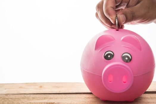 Hand is picking for coin up to drop into a piggy bank - Concept of saving money for the future