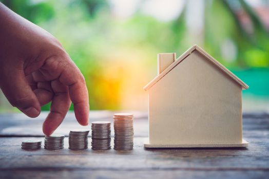 The hand that holds the coins is stacked and there is a house in the background. - The concept of saving for the future.