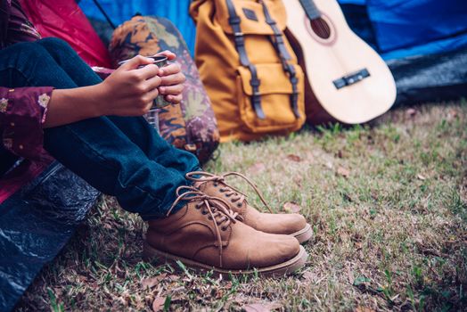 Young woman holding a glass of drink sitting in a tent in the morning nature.