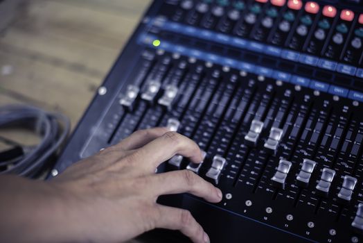 The DJ is adjusting the volume of the sound. Professional audio mixing console
