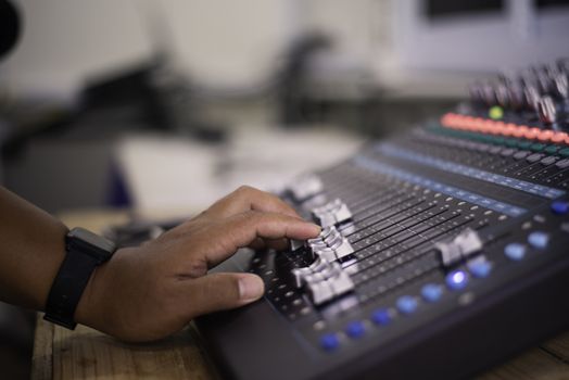 The DJ is adjusting the volume of the sound. Professional audio mixing console