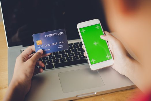 Hand holding a credit card in their hands and find information about a product using their mobile device to make purchases online and conduct financial transactions.