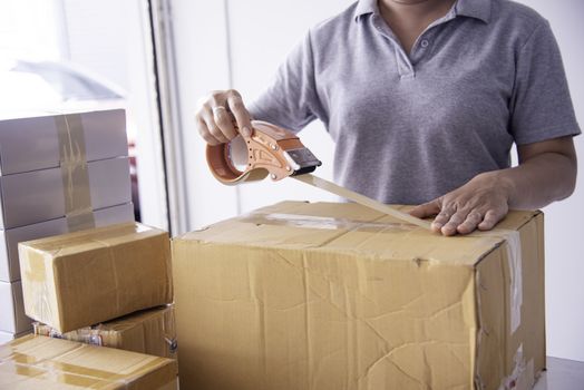 The staff is using the tape to pack the package goods to the customer.