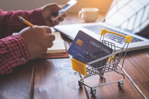 Small shopping cart with credit card inside and behind is business on desk - concept use credit for shopping.