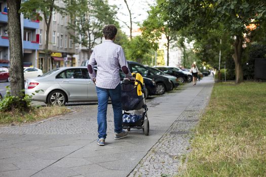 Young dad walking with a baby carriage on urban sidewalk