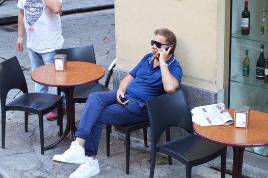 Man in sunglasses sitting in outdoor cafe enjoying free time talking on mobile phone, Italy, Sicily, Palermo, October, 8, 2018.