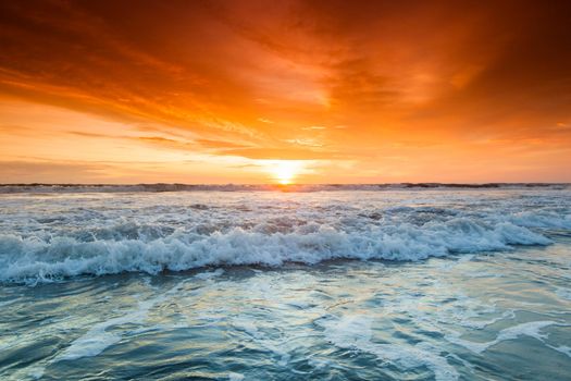 Splashing ocean wave in front of beautiful sunset sky background