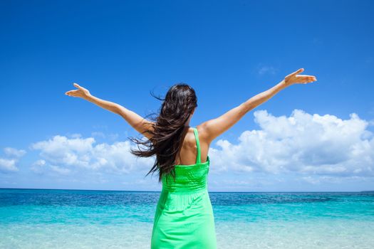 Woman in green dress posing in tropical sea beach with arms raised