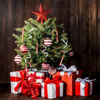 Decorated Christmas tree with candy canes , star , striped baubles and gift boxes on wooden background