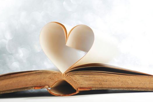 Pages of open book rolled in heart shape on glitter background