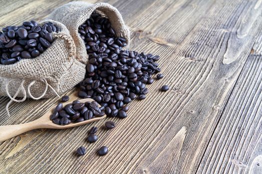 Close up stack of coffee bean on wooden spoon and in brown sack place on wooden background with copy space. Coffee bean full of sack as abundant. Food and drink concepts.