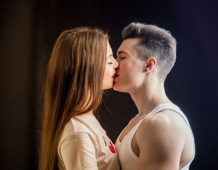 Romantic couple kissing in studio shot, man is muscular, woman is long-haired and wearing white t-shirt
