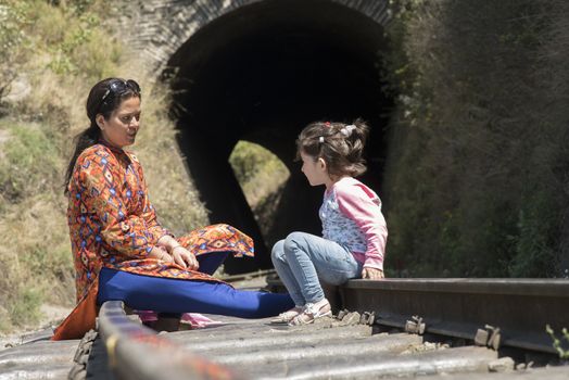Mother and daughter sitting on a rail track, talking.