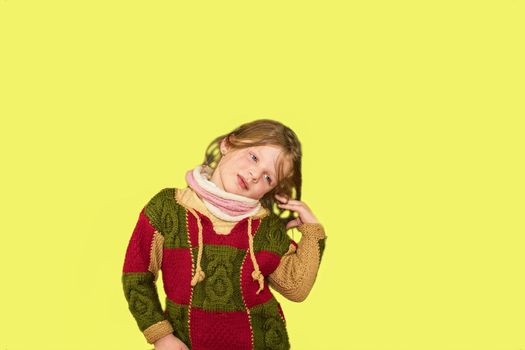 Little girl on colourful background. Copy space. Young girl is wearing sweater. Soft yellow background.