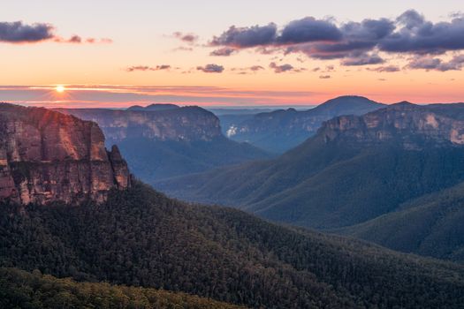 Scenic views across the Grose Valley as it appears to zig zag through the cliffs.  The sun colouring up the clouds and tingeing underbelly of some others.  