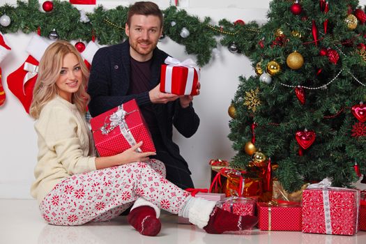 Couple in love sitting next to a nicely decorated Christmas tree, hloding Christmas gifts and smiling