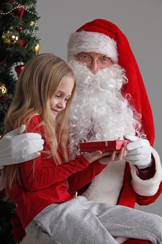 Portrait of smiling little girl sitting on santa claus knees and getting small gift