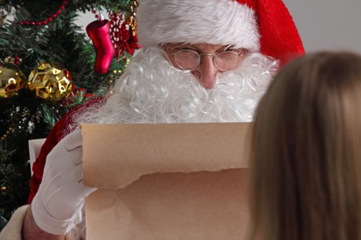 Santa Claus with with list or nice or naugthy list paper with small boy near christmas tree