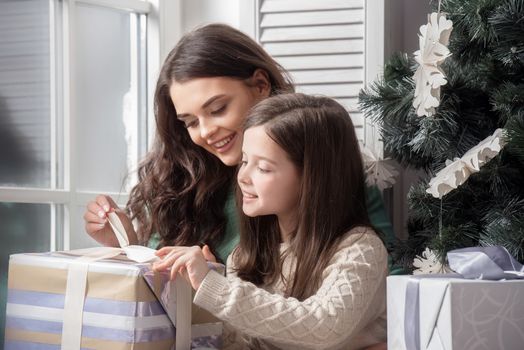 Mother and daughter unwrapping a gift sitting on the floor near christmas tree