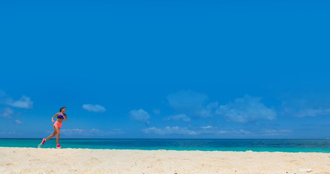 Young woman running on summer beach on the coast of the ocean blue sky background