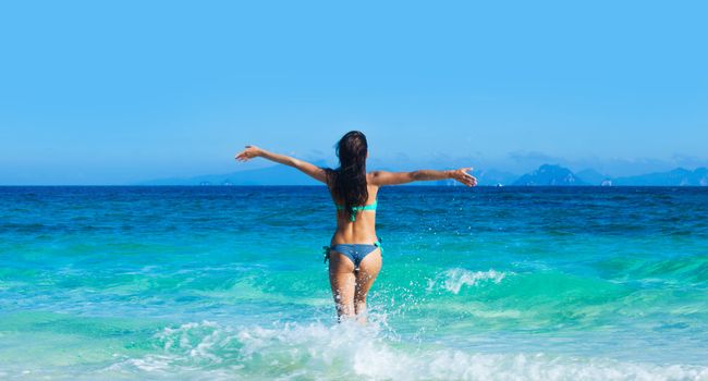 Beautiful woman in bikini run into blue tropical sea