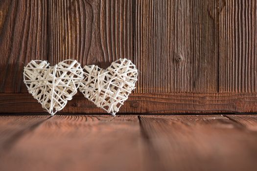 Two wicker hearts on brown wooden background
