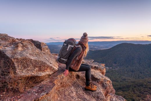 Female hiker with backpack rests on a mountain peak rocky ledge with magnificent views in Blue Mountains Australia