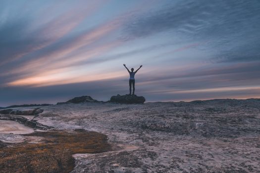Muted tones of the sunset skies from Lincolns Rock Kings Tablleland. A woman stands with windblown hair and arms outstretched to the sky in awe or praise