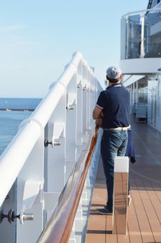 A man standing on the deck of a cruise ship and looking at the shore on a Sunny day, vertical shot.