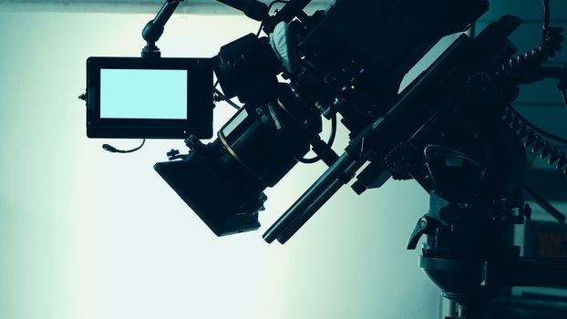 Silhouette images of video camera in tv commercial studio production which operating or shooting by cameraman and film crew team in set and prop on professional crane and tripod for easy to pan tilt or shift