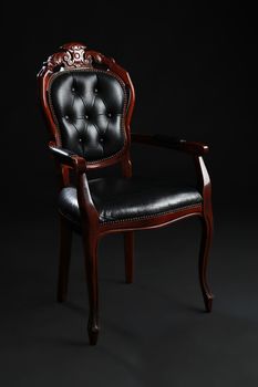 Old black chair, upholstered in leather on black background.