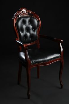 Old black chair, upholstered in leather on black background.