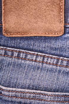 Leather label on denim jeans background, close up. Brown leather tag, double seams, strap on dark blue denim jeans. Leather frame with brown seam.